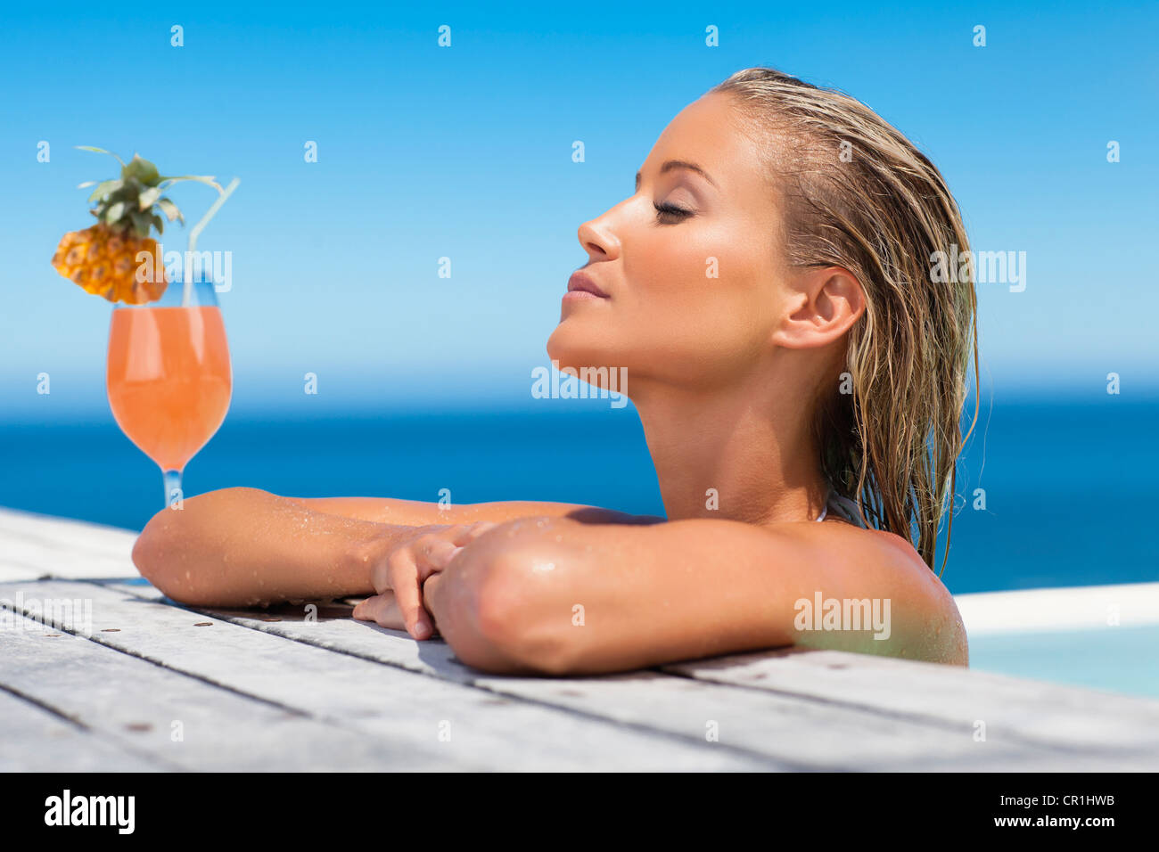 Donna di rilassarsi con drink in piscina Foto Stock