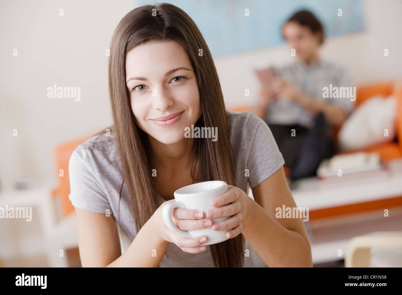 Stati Uniti, California, Los Angeles, Ritratto di giovane donna holding mug, uomo in background Foto Stock