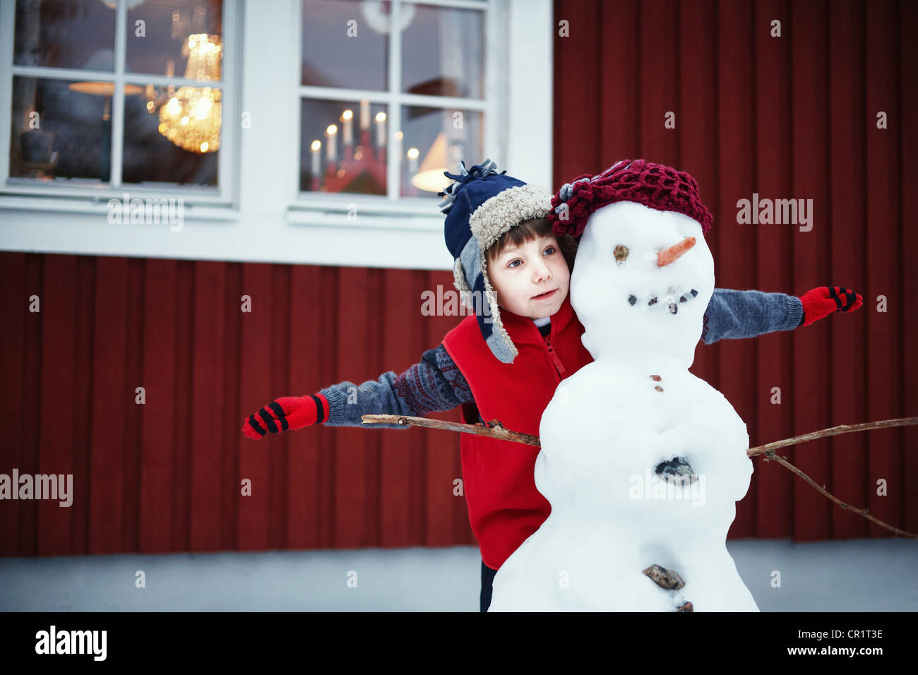 Ragazzo giocando con il pupazzo di neve all'aperto Foto Stock