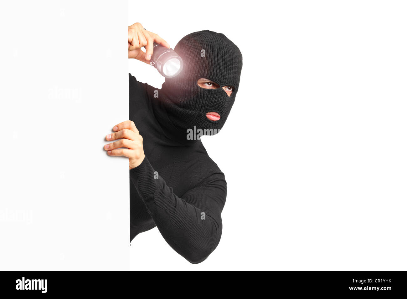 Un ladro con maschera di rapina tenendo una torcia dietro un pannello bianco isolato su sfondo bianco Foto Stock