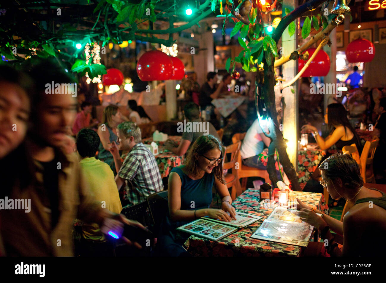 I turisti stranieri e backpackers mangiare e bere durante la notte in un bar esterno sul Soi Rambuttri vicino a Khao San Road, Bangkok Foto Stock