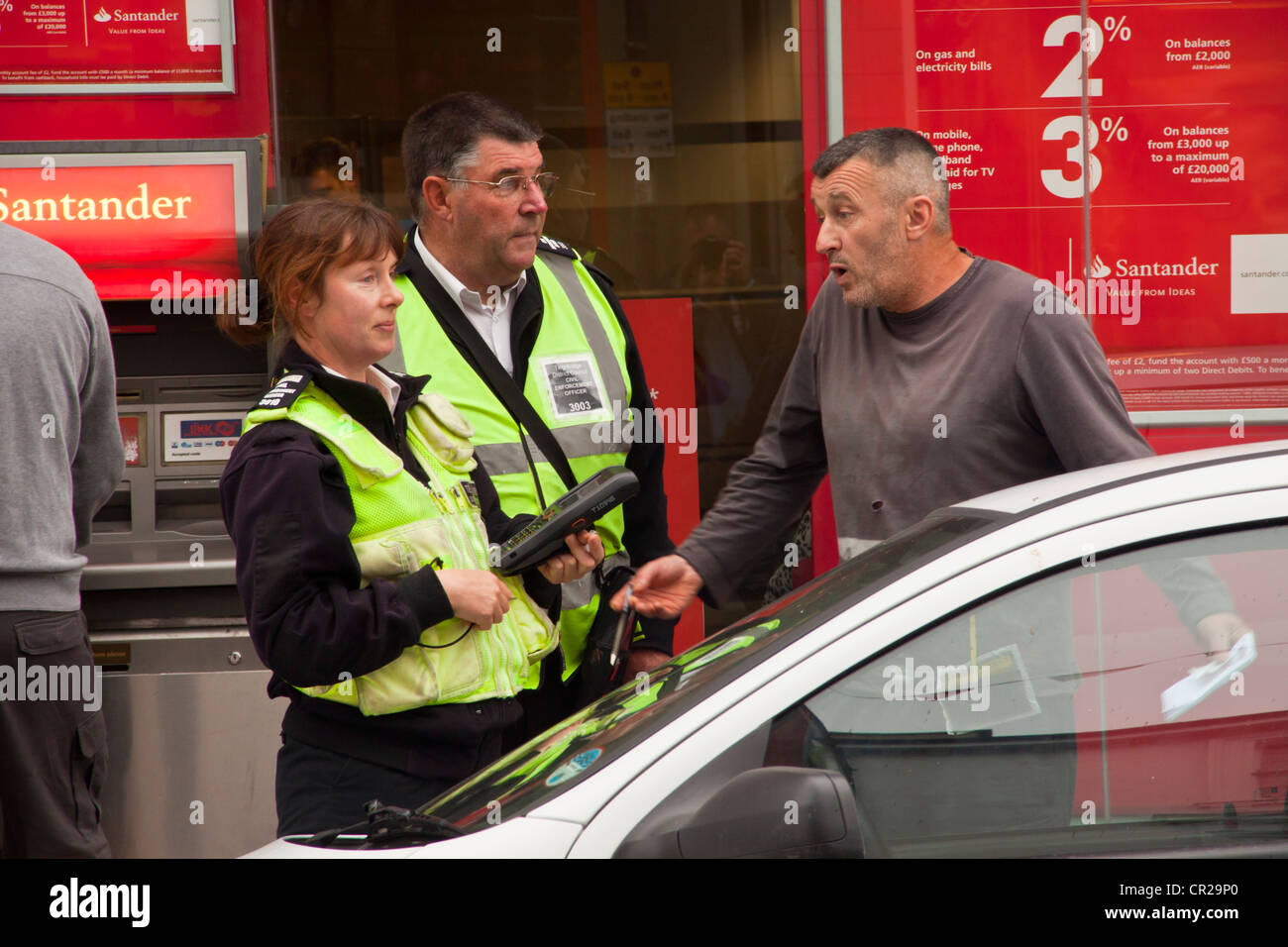 L'uomo sostenendo con il traffico operai sostegno comunitario ufficiali dopo i hes stati dato i biglietti per il parcheggio per il parcheggio è troppo lungo. Foto Stock