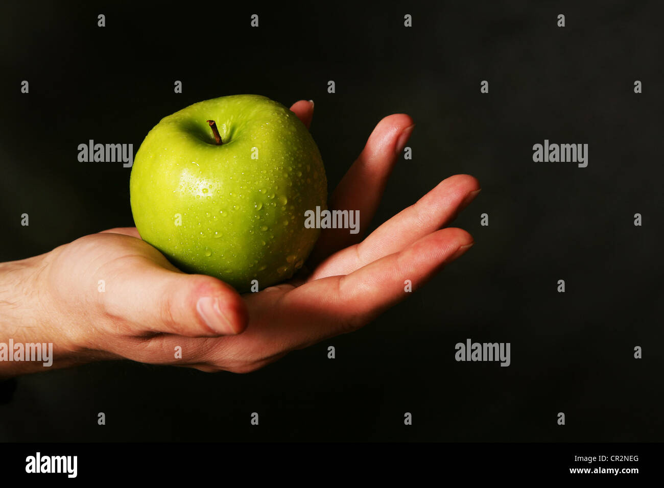 Mano d'uomo con una mela verde su sfondo scuro Foto Stock