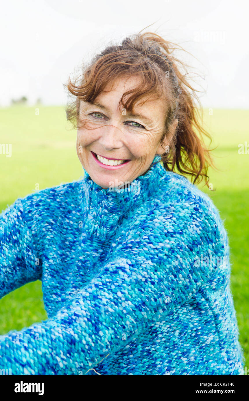 Un sorridenti donna matura seduto sull'erba e indossa un maglione blu Foto Stock
