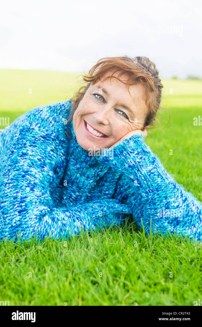 Un ritratto di un sorridenti donna matura nei suoi anni quaranta che indossa un maglione blu e posa sull'erba. Foto Stock