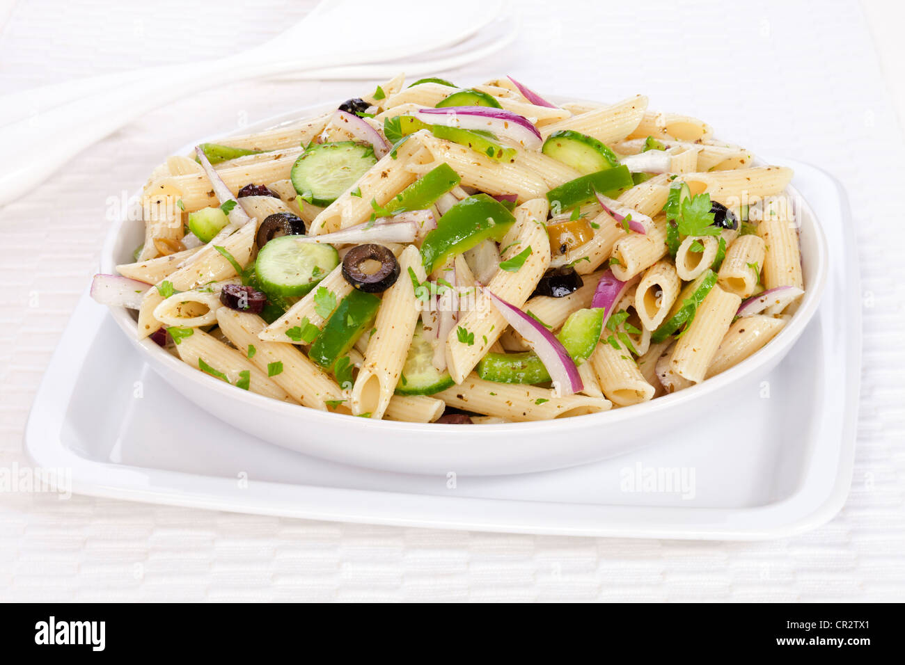 Un vegetariano insalata di pasta con un pesto di basilico medicazione, olive, cipolla rossa, il cetriolo e il peperone verde, cosparsa di prezzemolo. Foto Stock
