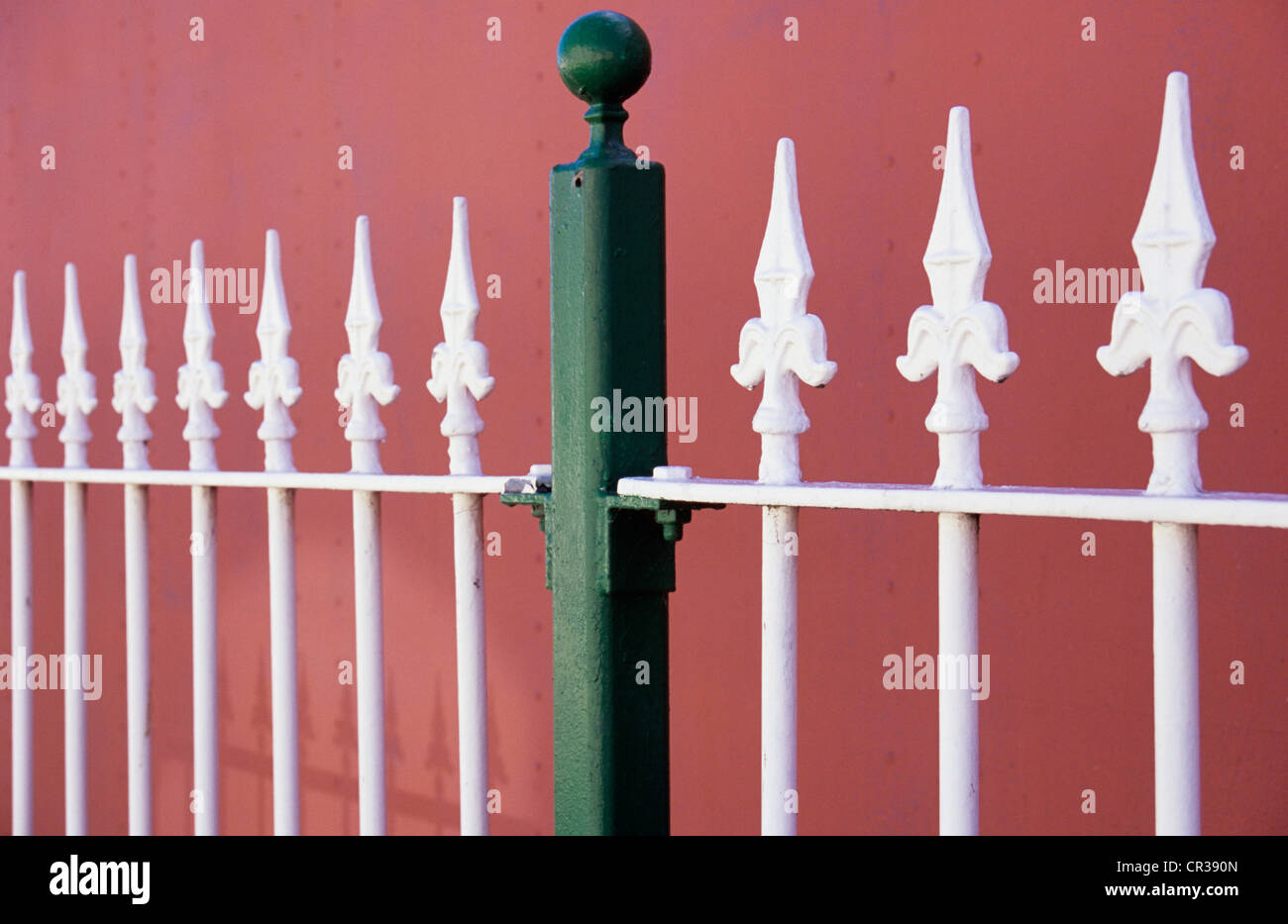 Metallo verde post con manopola di supporto di metallo bianco ringhiere e rabboccato con fleurs-de-lys nella parte anteriore della parete dipinta di colore rosa salmone Foto Stock