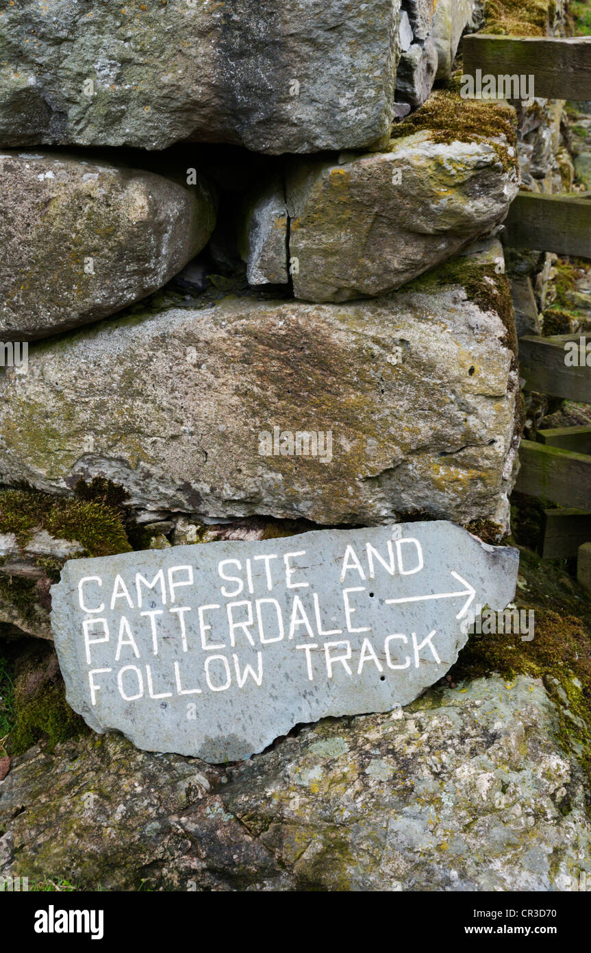 Campeggio e le direzioni di segno Patterdale sull'ardesia fissata a secco muro di pietra. Foto Stock