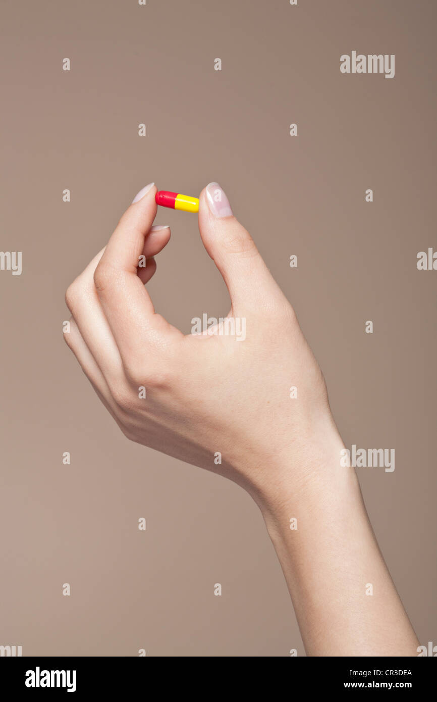 La mano di una giovane donna che mantiene una pillola, capsula tra le dita Foto Stock