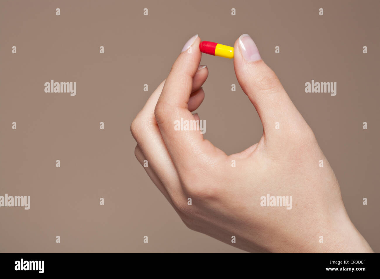 La mano di una giovane donna che mantiene una pillola, capsula tra le dita Foto Stock