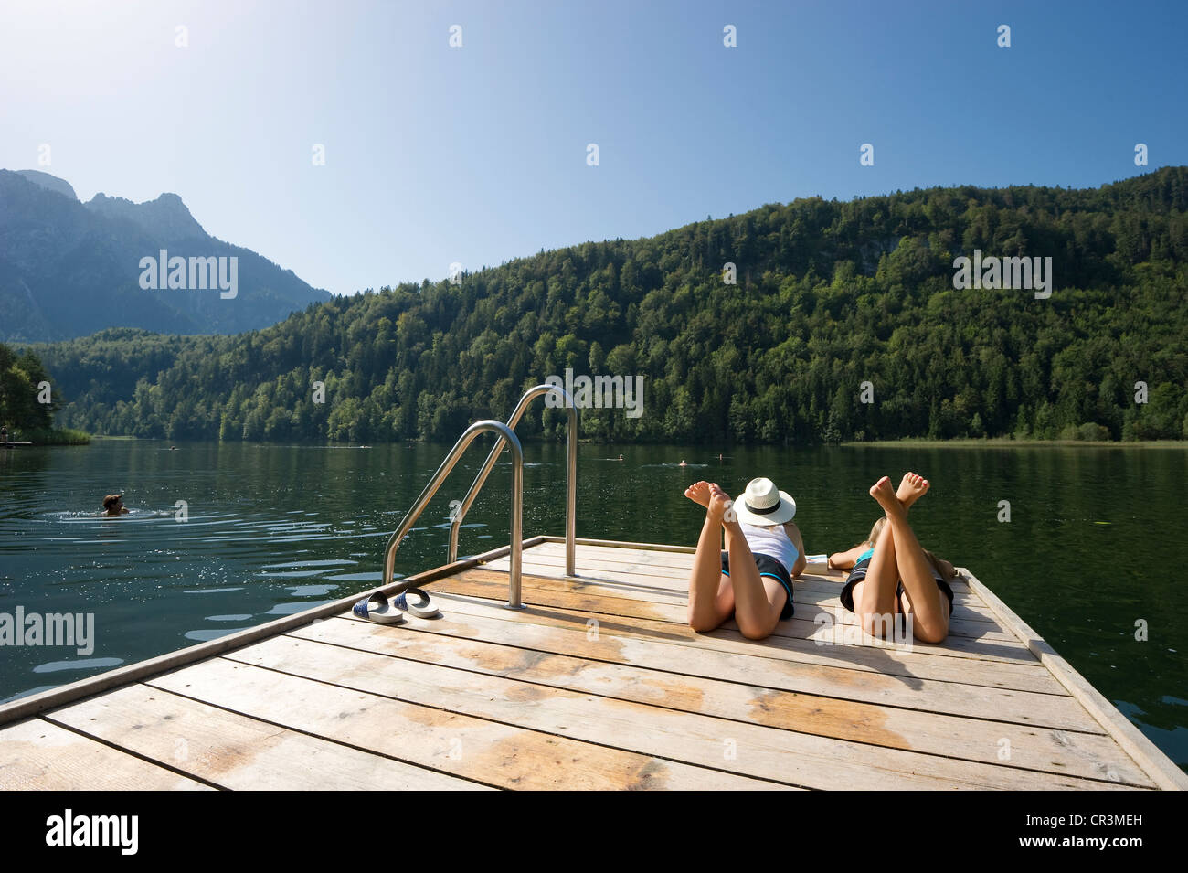 Le giovani donne che giace su di un pontile sul lago Schwansee vicino a Füssen, Allgaeu regione Baviera, Germania, Europa Foto Stock