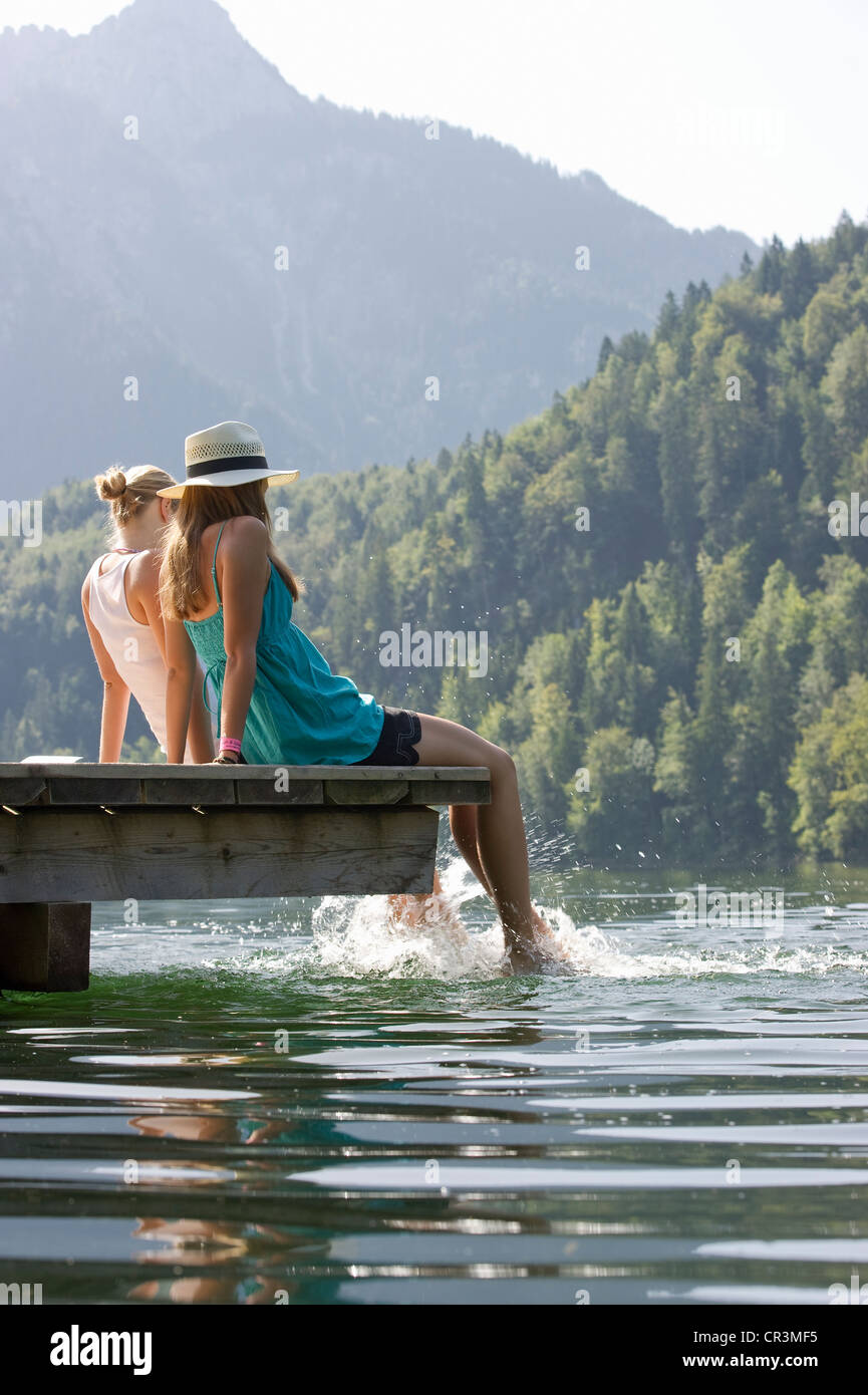 Giovane donna seduta su un pontile sul lago Schwansee vicino a Füssen, Allgaeu regione Baviera, Germania, Europa Foto Stock