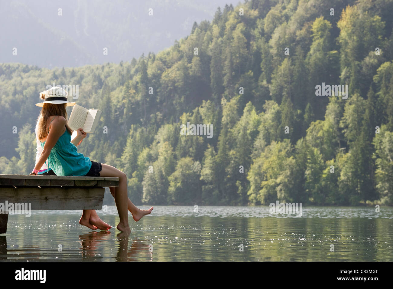 Giovane donna seduta su un pontile sul lago Schwansee vicino a Füssen, Allgaeu regione Baviera, Germania, Europa Foto Stock