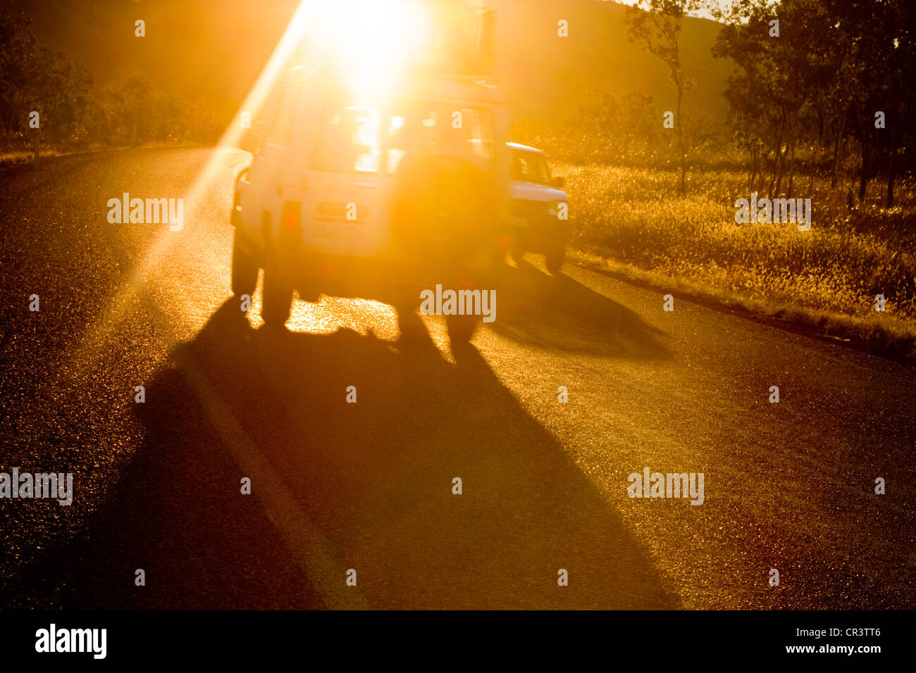 Due veicoli che transitano su di una curva al tramonto, Sun sta versando in foto. Una leggera sfocatura di movimento. Foto Stock