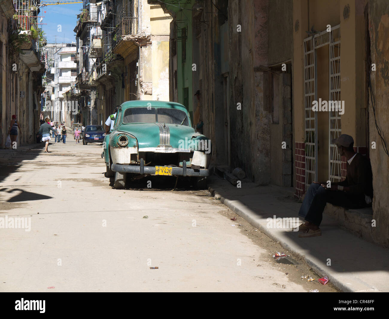 Scena di strada con un uomo seduto presso la porta anteriore ed un cubano di auto d'epoca naufragare in Old Havana, Cuba, America Latina Foto Stock