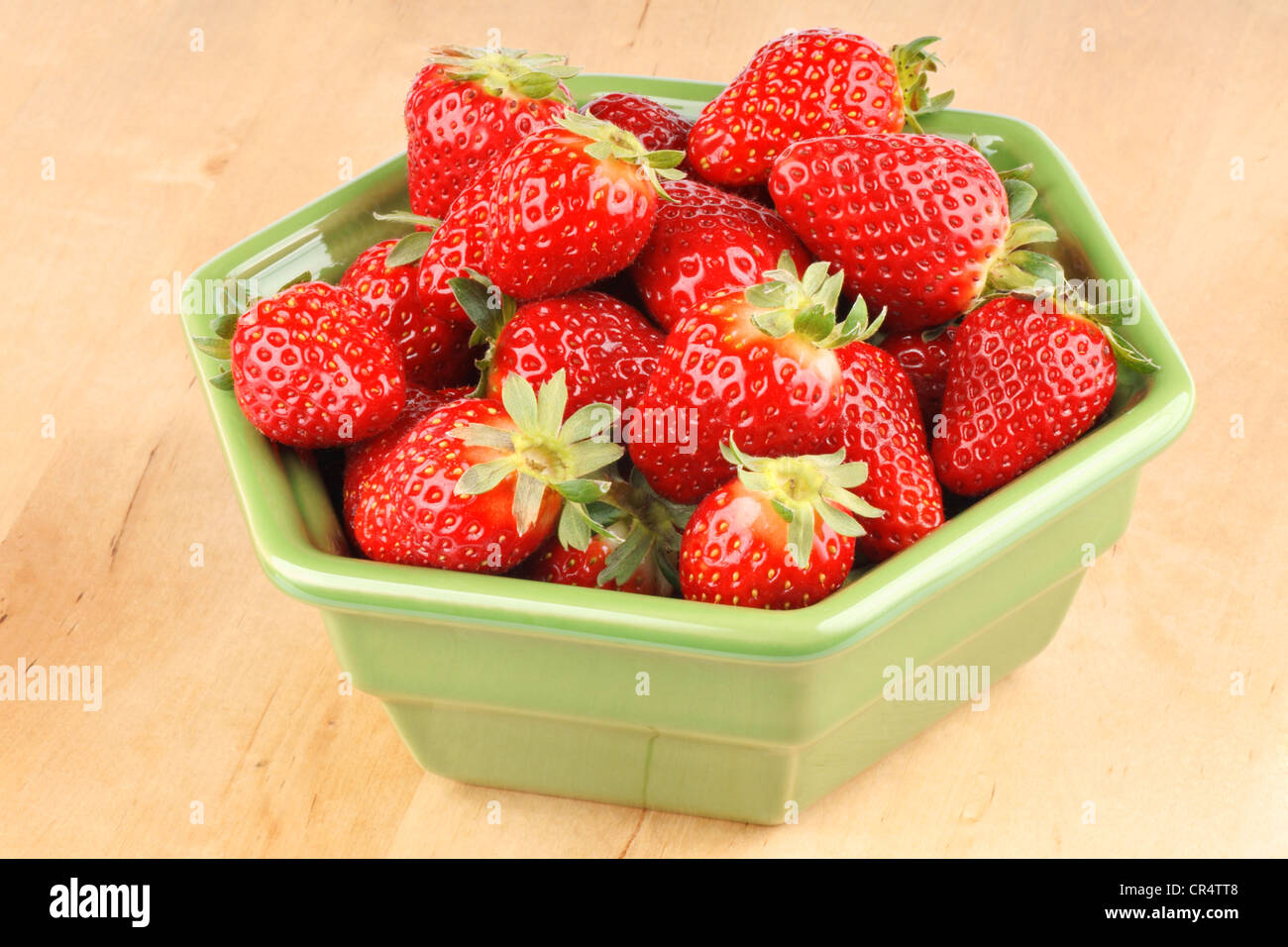 Fresche fragole mature nel verde di un vaso in ceramica su uno sfondo di legno Foto Stock