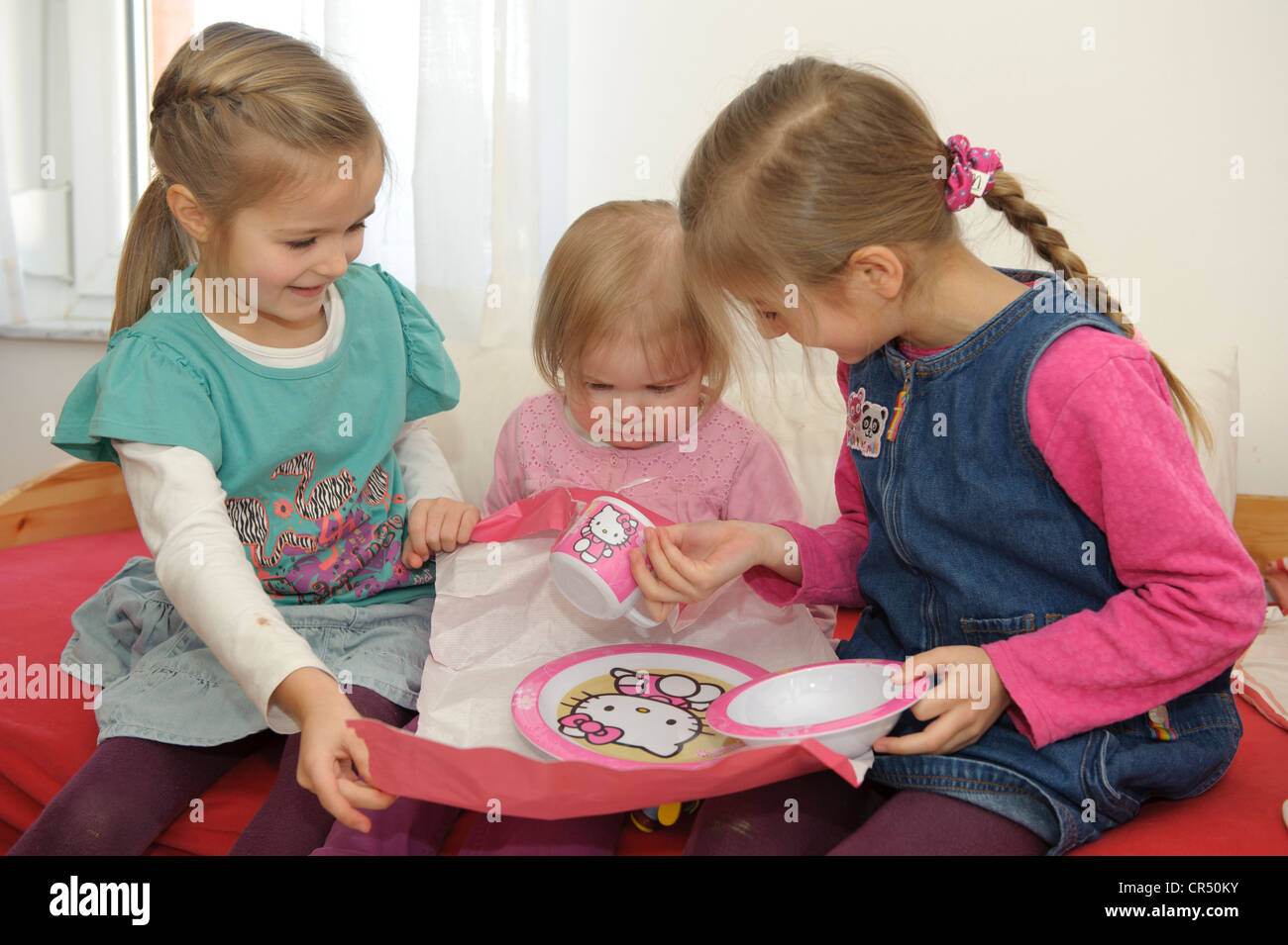 Due sorelle, di 5 e 6 anni, aiutando i loro sorellina, 2 anni, scartare un regalo Foto Stock