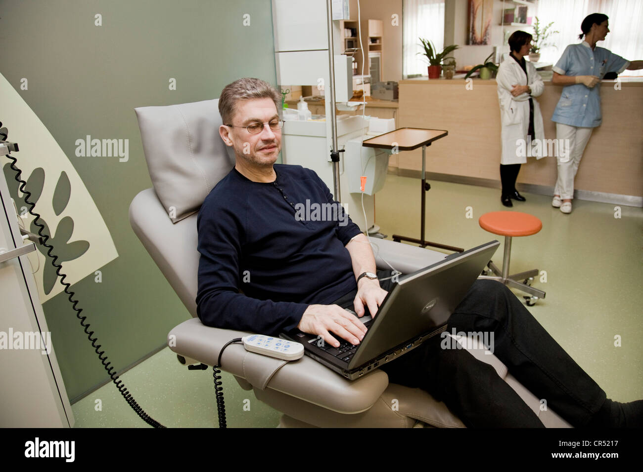 Paziente seduto su una sedia di trattamento al lavoro su un notebook durante un trattamento chemioterapico, oncologia clinica privata Foto Stock
