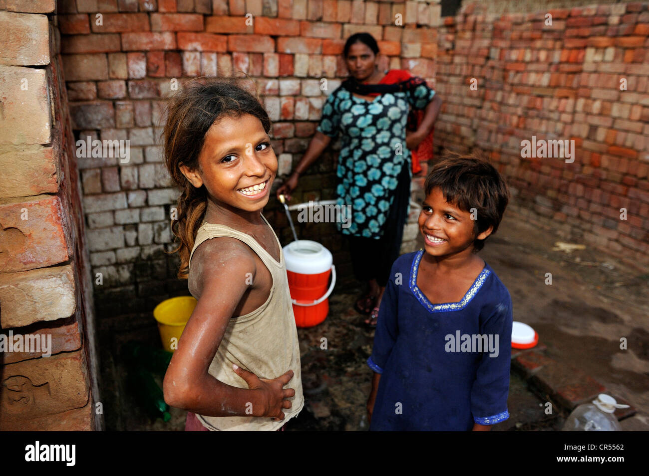 Donna e ragazze raccolta di acqua da un rubinetto, vivono e lavorano con la loro famiglia sotto la schiavitù-come pratica del debito Foto Stock