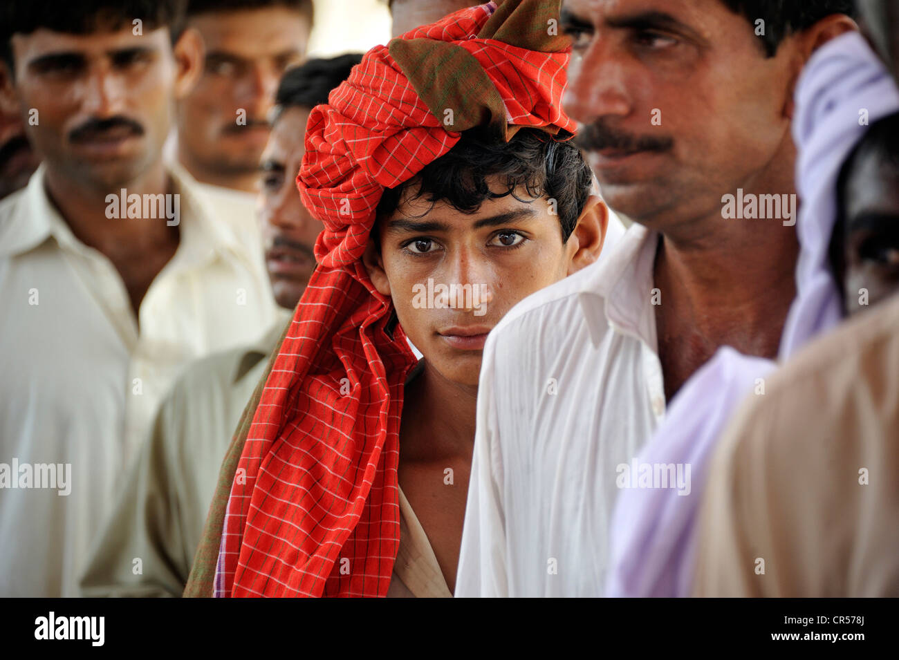La gioventù che indossa un panno rosso sul suo capo e gli uomini durante la distribuzione di beni da parte di un'organizzazione di beneficenza dopo il diluvio Foto Stock