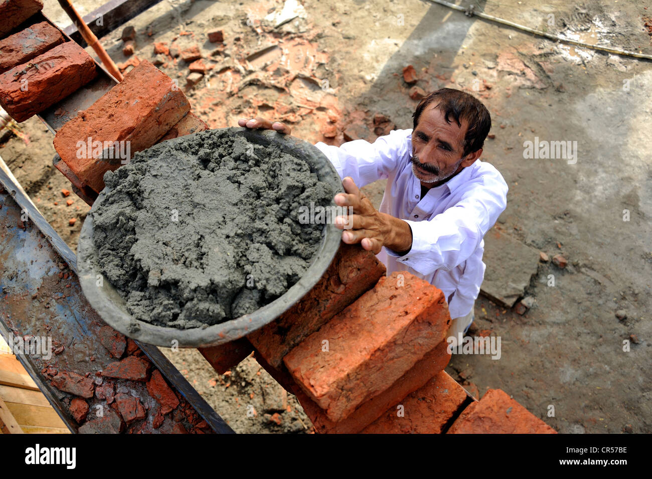 L'uomo della coppa di sollevamento con cemento su una impalcatura, la costruzione di case di mattoni per le famiglie le cui case sono state distrutte durante la Foto Stock