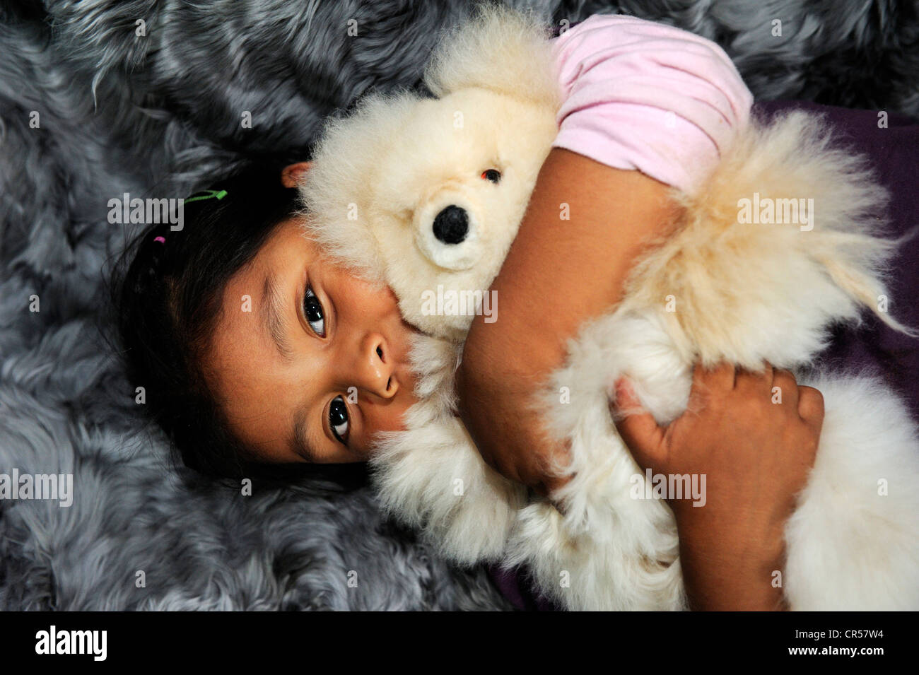 Ragazza con indigeni caratteristiche facciali che abbraccia un orsacchiotto di peluche, produzione di giocattoli morbidi e tappeti dal pelo di alpaca in una piccola famiglia Foto Stock