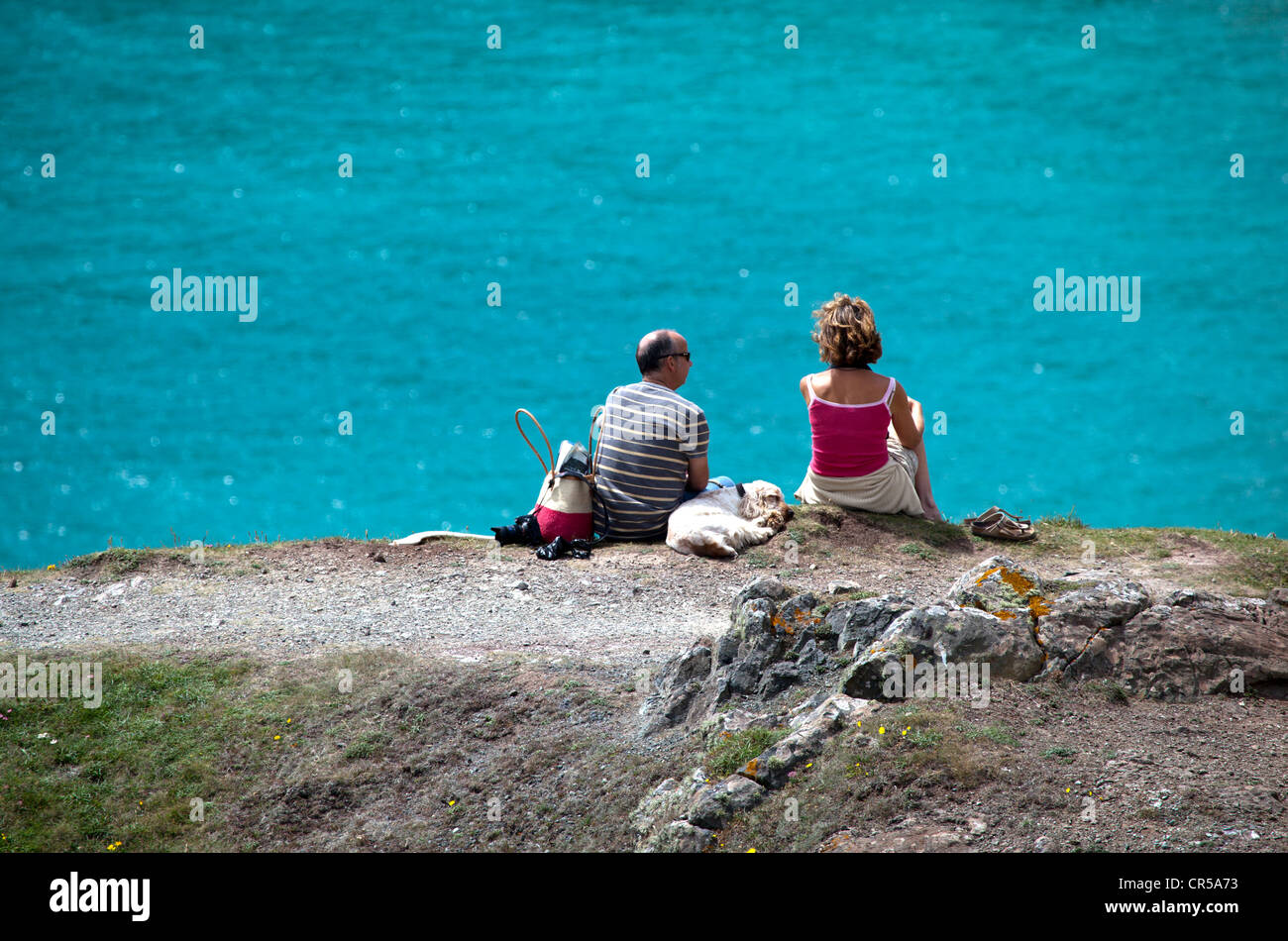 Giovane con cane seduto su una scogliera sopra Kynance Cove Foto Stock