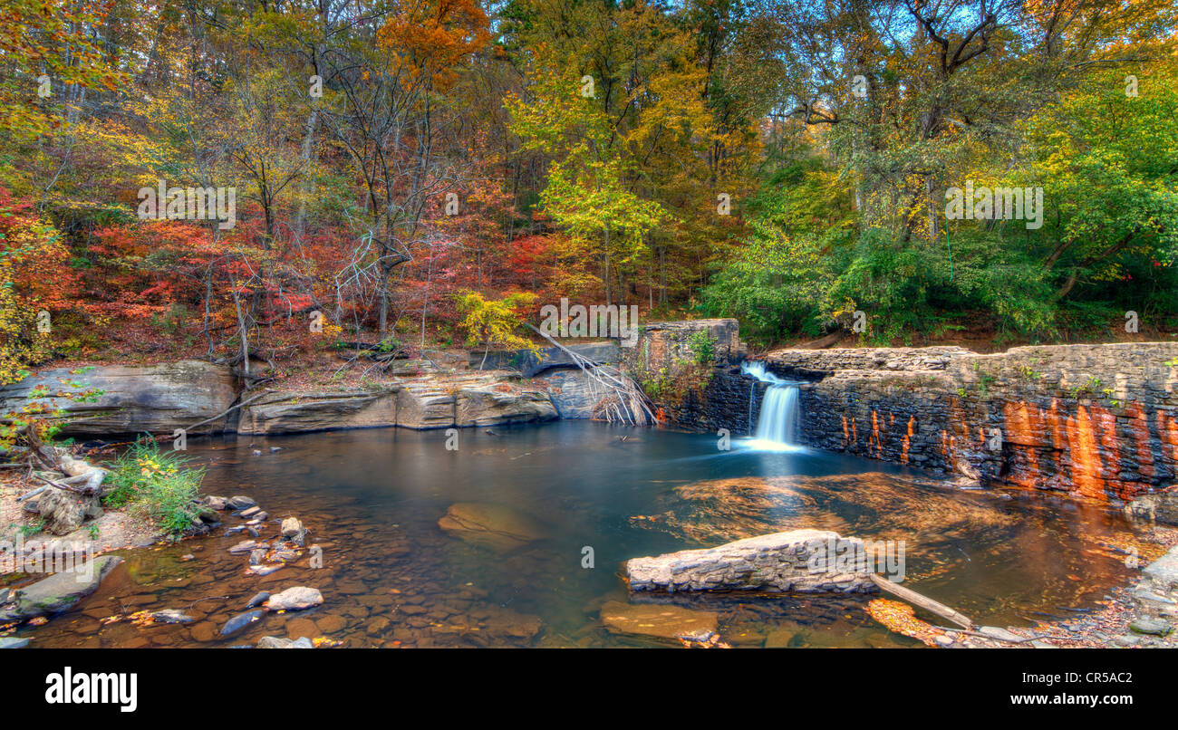 Una piccola cascata in la rottura di una diga circondato da inizio di caduta foglie. Foto Stock