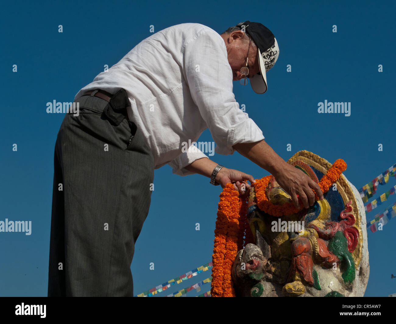 Uomo locale che offre una ghirlanda di fiori in un'immagine di una dea, Boudnath, Kathmandu, Nepal, Sud Asia Foto Stock