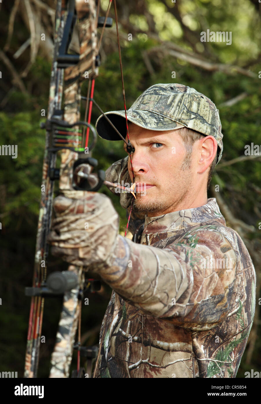 Close-up bow hunter vestito in camuffamento tirando arco tornare nel bosco Foto Stock