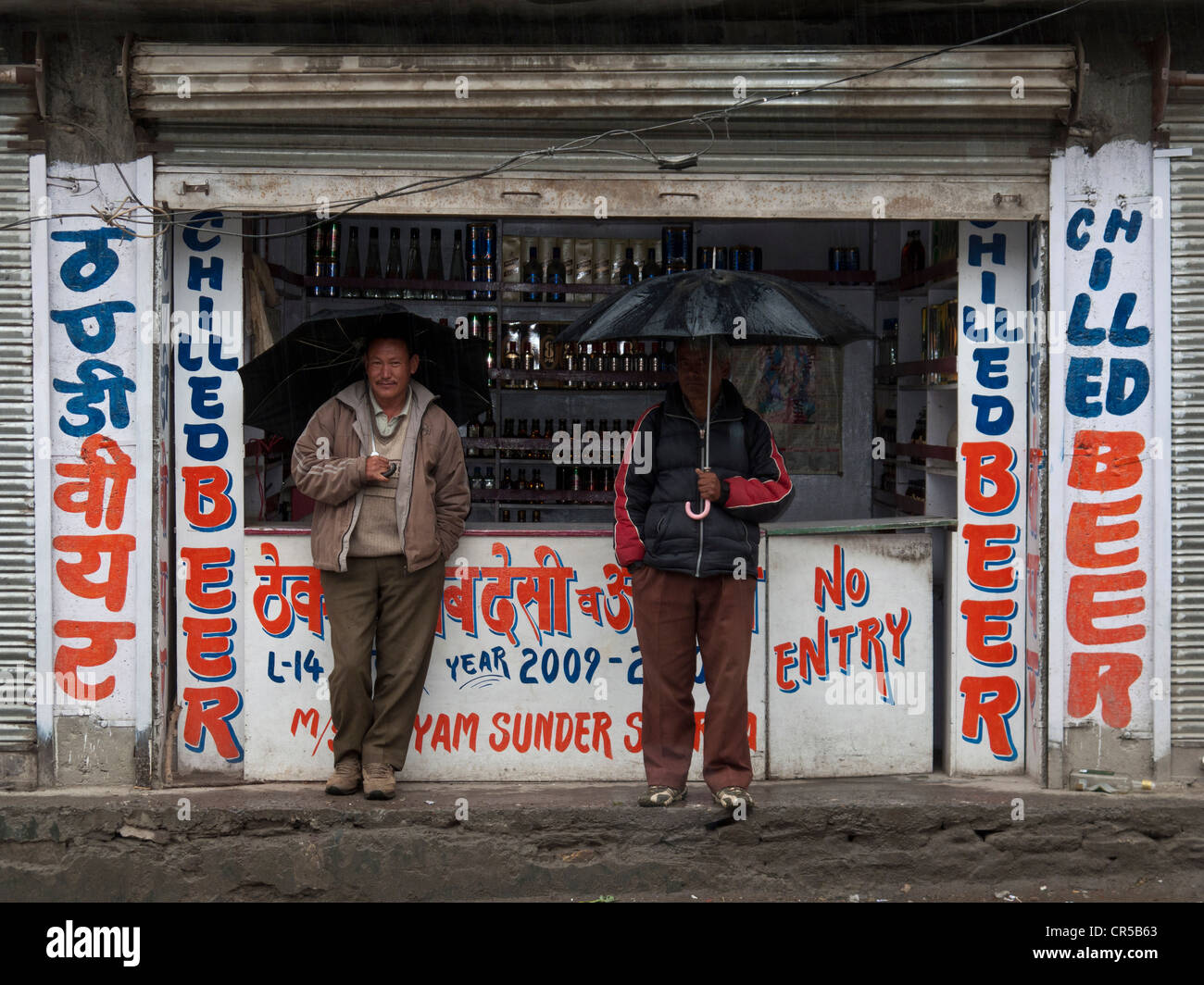 Due uomini di prendere rifugio in un negozio di liquori, aspettando la pioggia per arrestare, Sissu, Himachal Pradesh, India, Asia Foto Stock