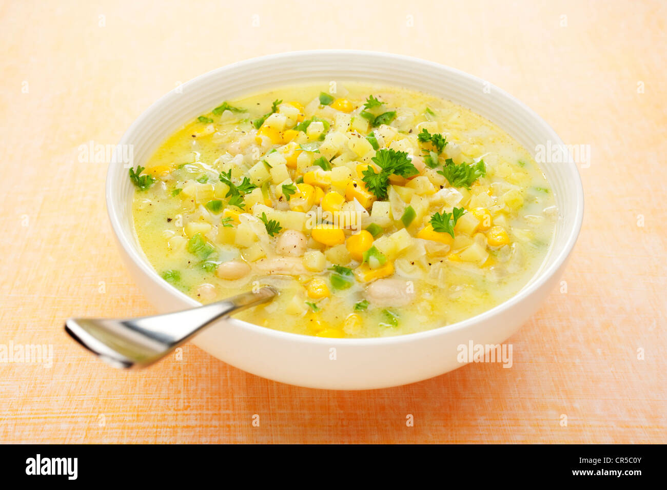 Una ciotola di zuppa di mais con patate e peperoni verdi, su un pallido sfondo arancione. Foto Stock
