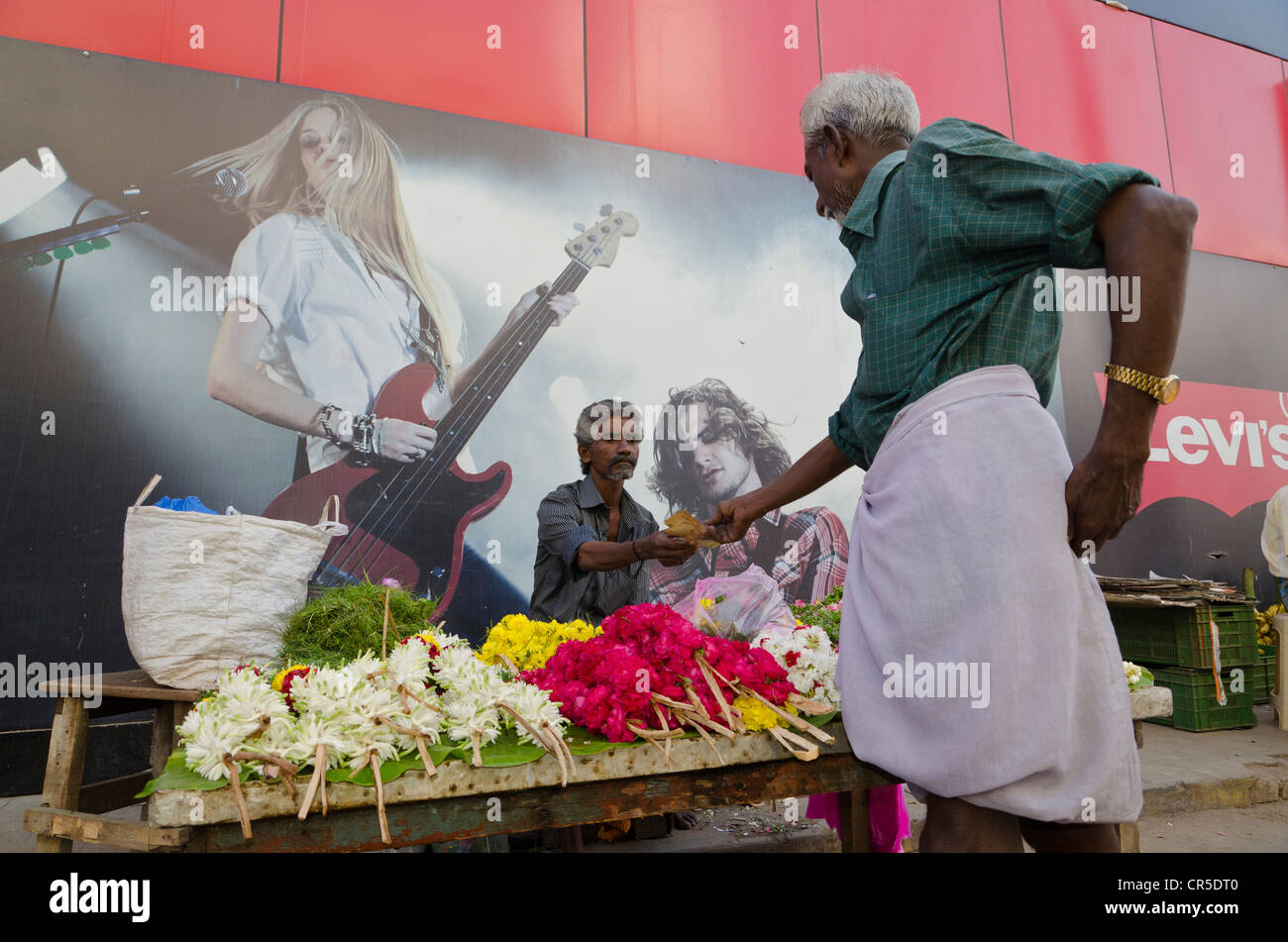 Flowerseller con il suo negozio di impostare nella parte anteriore di un concerto di poster, Madurai, Tamil Nadu, India, Asia Foto Stock