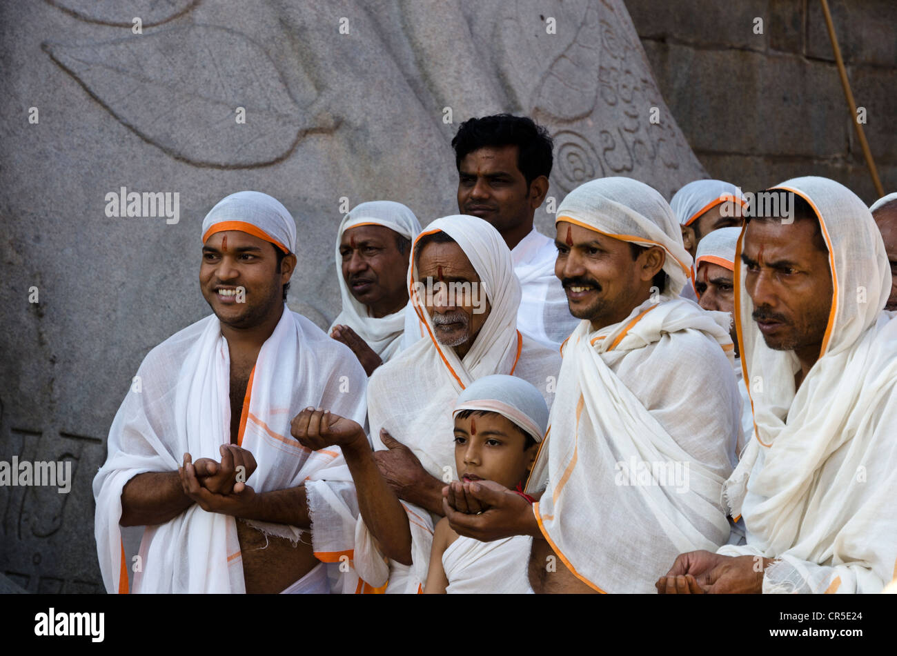Un gruppo di pellegrini di Jain è recitare testi religiosi ai piedi della gigantesca statua di Gomateshwara in , India, Asia Foto Stock