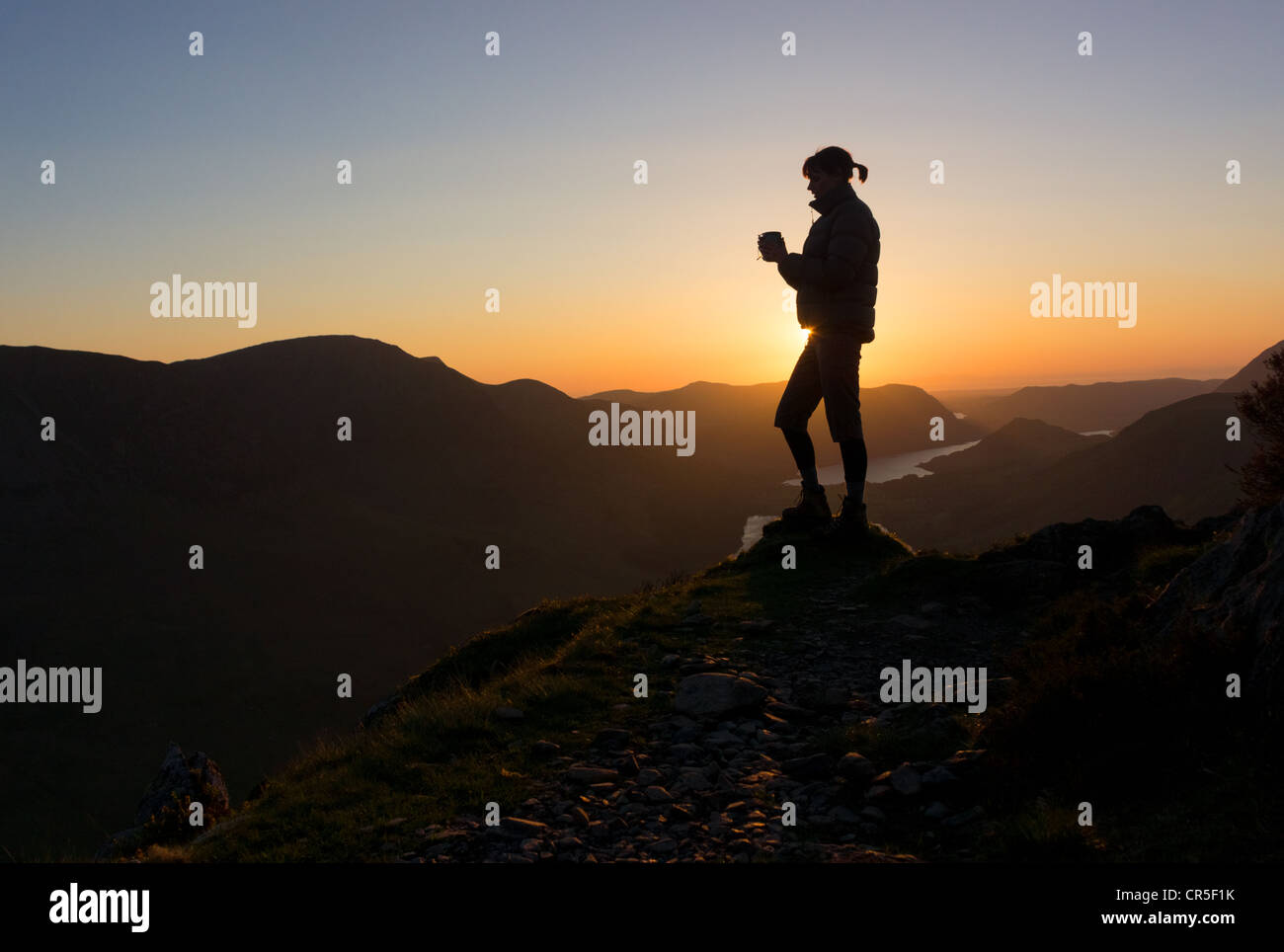 Una donna si affaccia verso Haystacks nel Lake District in Cumbria mentre vi gustate una bevanda calda al tramonto. Foto Stock