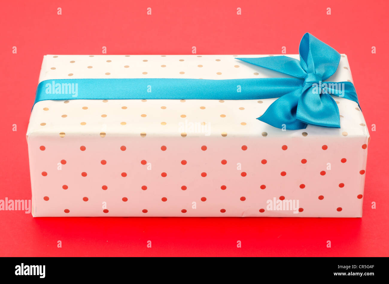 Gift Wrapped box con un nastro di colore blu e la prua - sparato in studio con uno sfondo rosso Foto Stock
