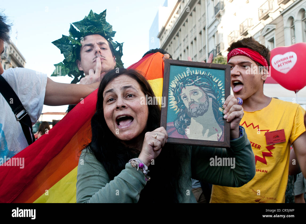 Omosessuali rendendo il divertimento di anti gay predicazione donna con un icona di Gesù nelle sue mani all'annuale di Atene Gay Pride Parade Foto Stock