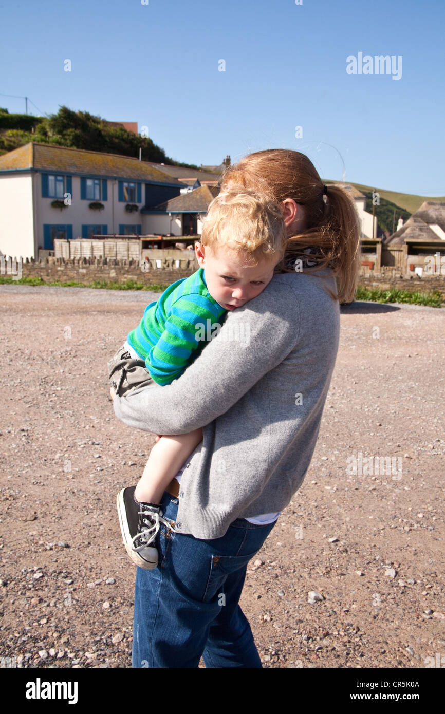 La madre che porta a due anni, baby boy, Speranza Cove, Devon, Inghilterra, Regno Unito. Foto Stock