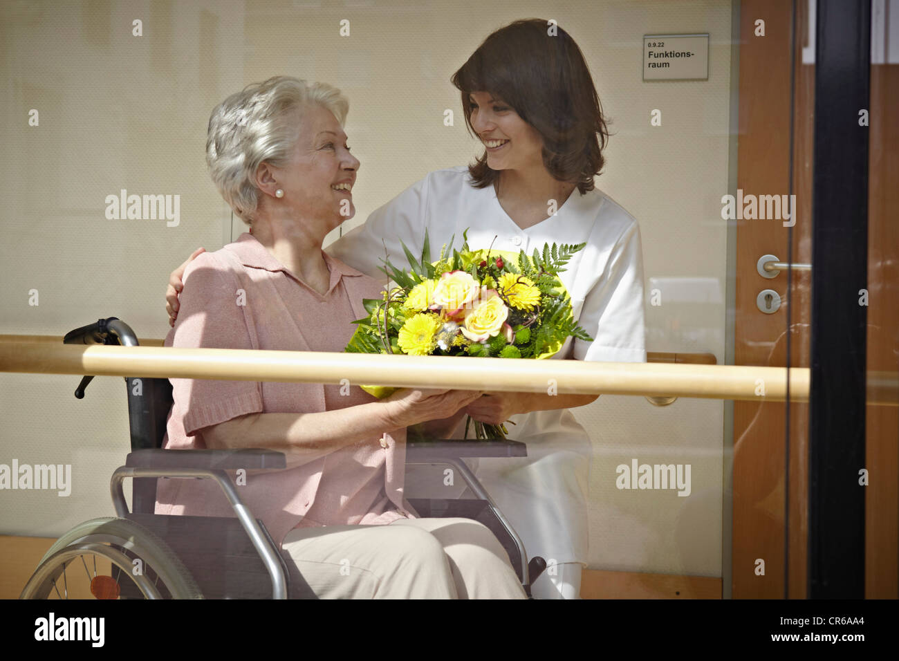 Germania, Colonia, il Custode dando mazzo di fiori per le donne anziane su una sedia a rotelle in casa di cura Foto Stock