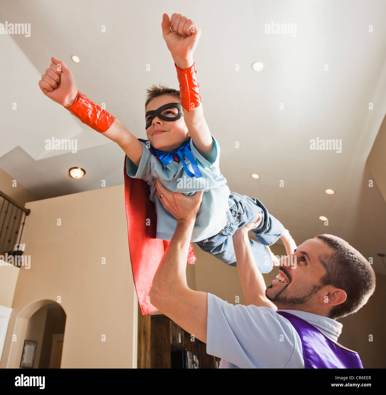 Padre holding aloft suo figlio (8-9) vestito in abiti fantasiosi costumi Foto Stock