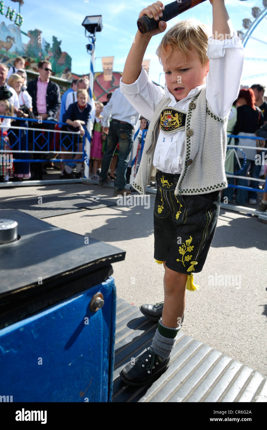 5 anno di old boy indossando il tradizionale pantaloni di pelle e camicia di colpire un martello su una prova di forza di gioco di divertimento Foto Stock