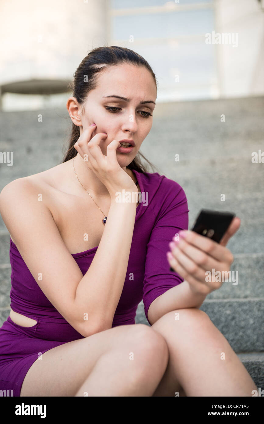Giovani preoccupato e nervoso donna tenendo il telefono cellulare e mordere le unghie Foto Stock