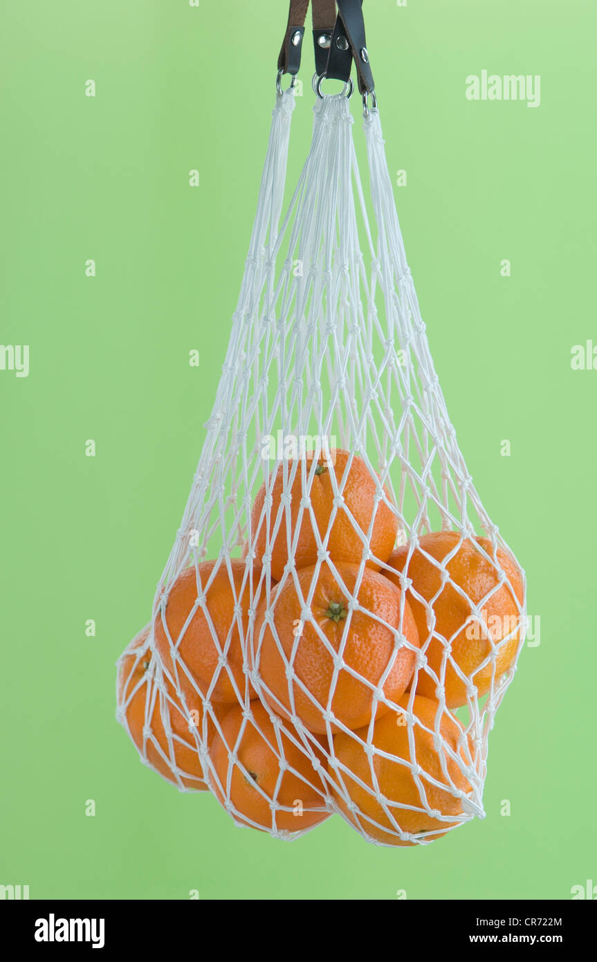 Arance in borsa a rete contro lo sfondo di colore verde, vicino fino Foto Stock