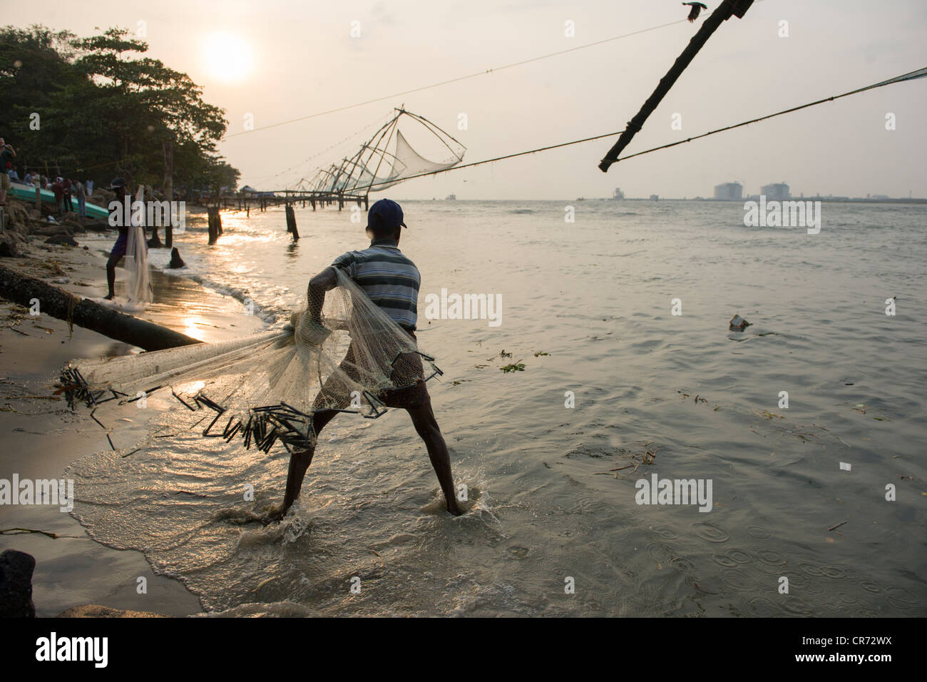L'uomo la colata di una rete da pesca accanto alla Cinese reti da pesca al tramonto, Fort Cochin, Kochi (Cochin), Kerala, India Foto Stock
