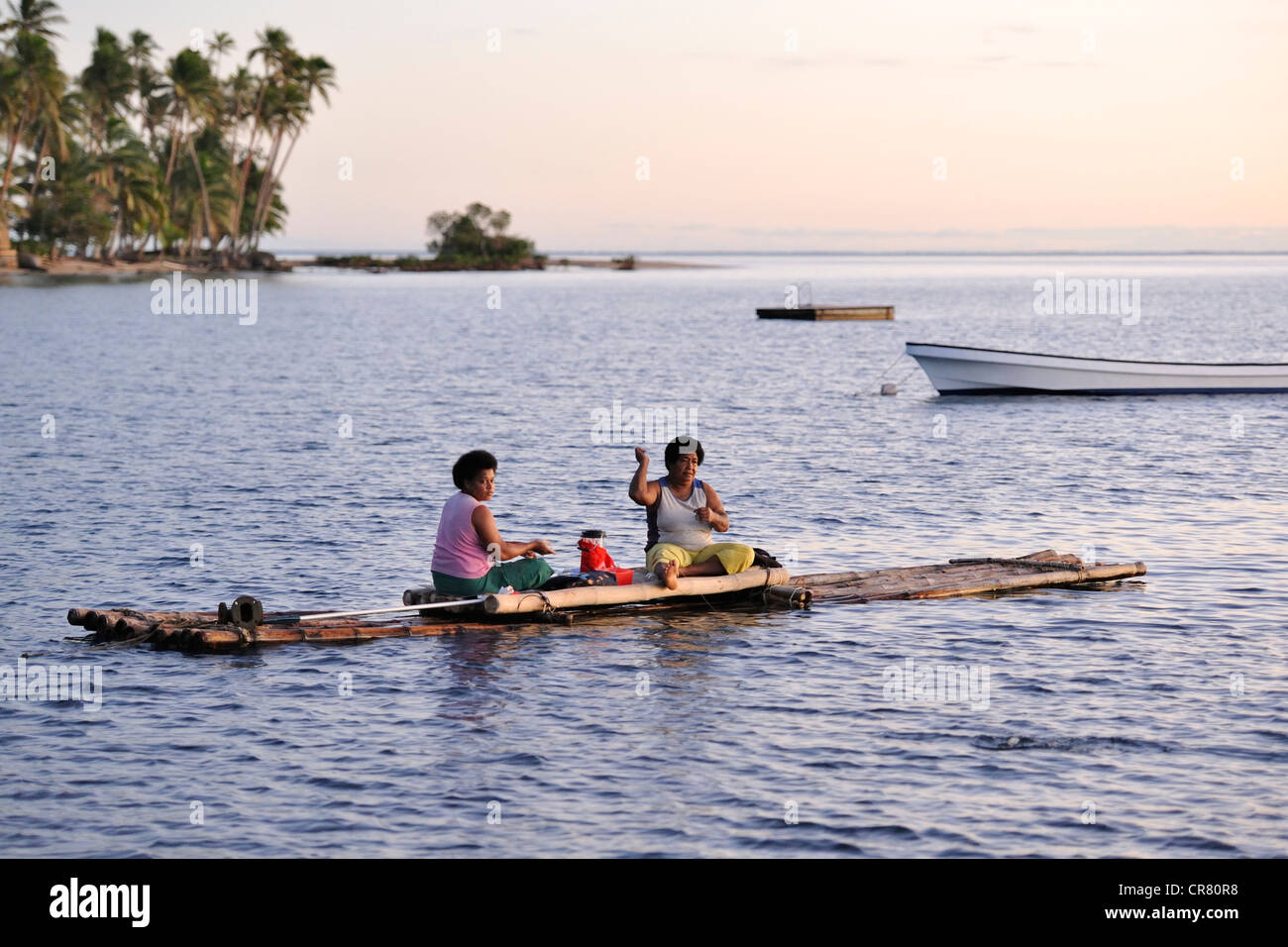 Due donne con una seduta chlid la pesca da un bambù canoa, nel tardo pomeriggio nei pressi di una sistemazione di resort. Savusavu Bay, Venua Levu. Fiji, Sud Pacifico Foto Stock