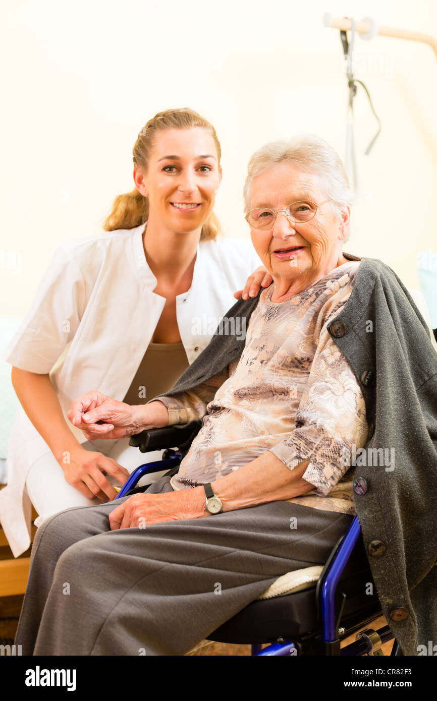 Infermiere Giovani e Senior Femminili in casa di cura, la vecchia signora seduta su una sedia a rotelle Foto Stock