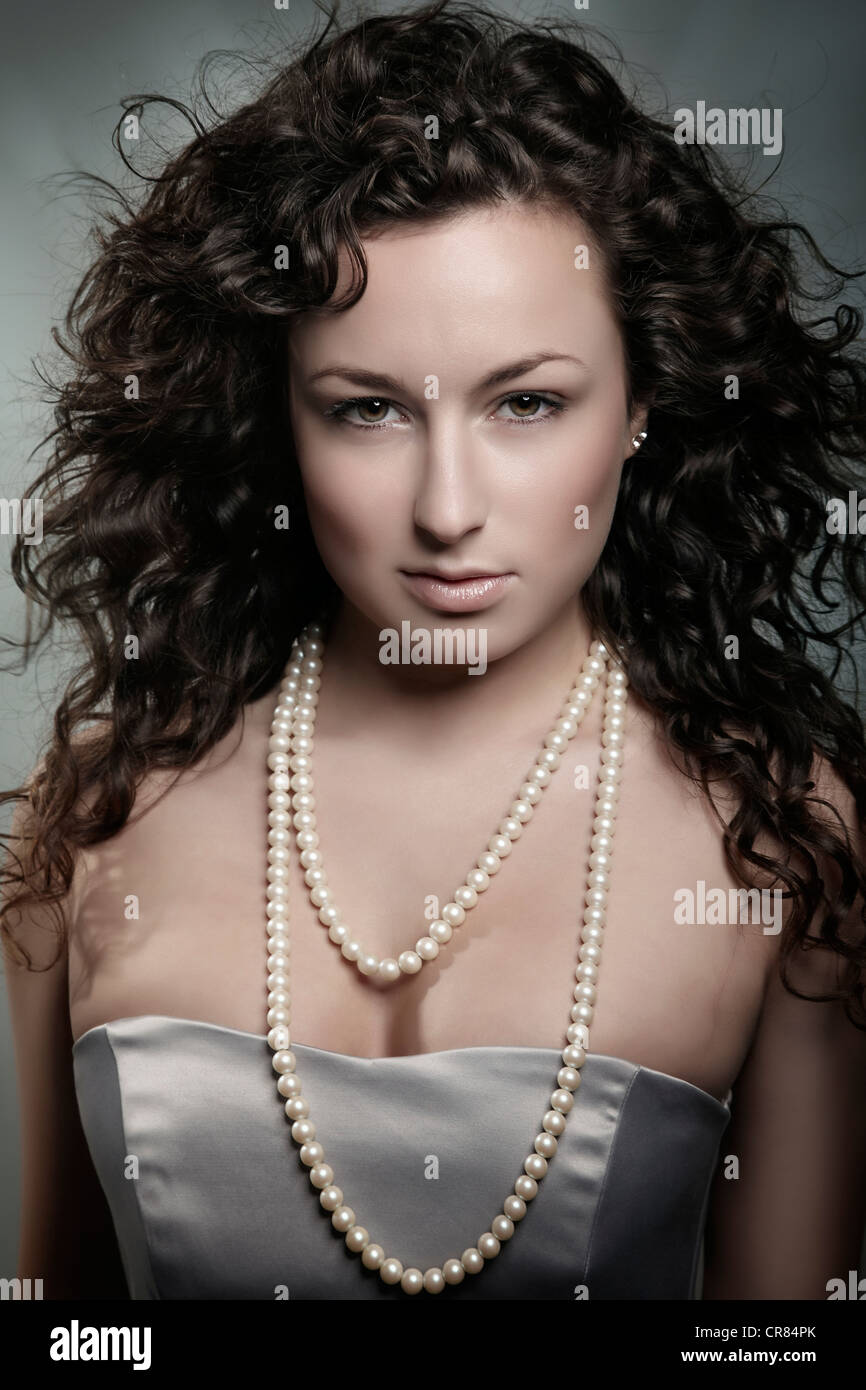 Giovane donna con ricci capelli marroni e collana di perle, ritratto di bellezza Foto Stock