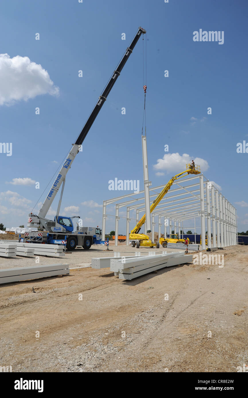 Sito di costruzione di un nuovo magazzino con gru mettendo travi metalliche nel terreno, Regensburg, Baviera, Germania, Europa Foto Stock