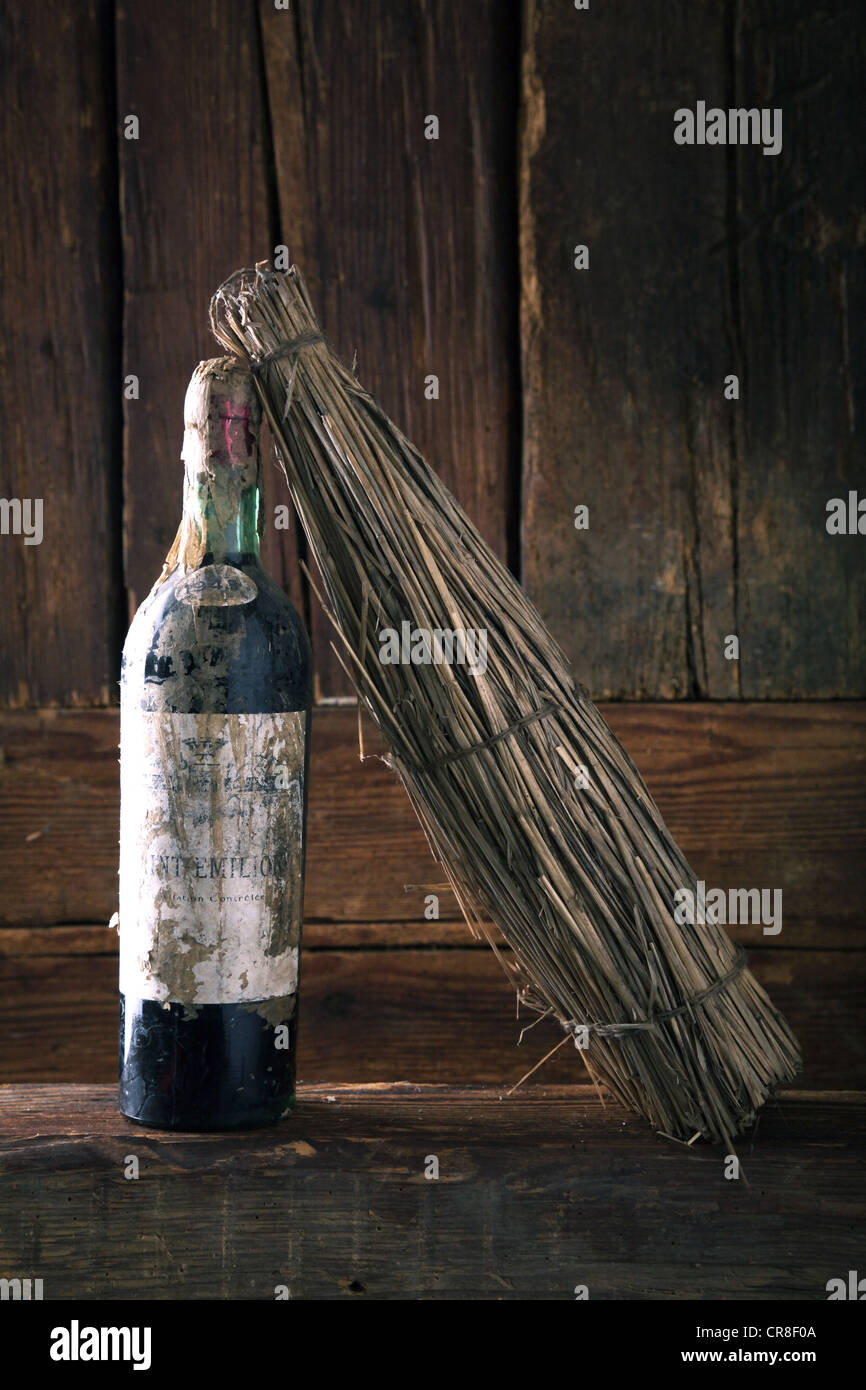 Vecchia bottiglia di vino rosso con paglia caso davanti ad un rustico di parete in legno Foto Stock