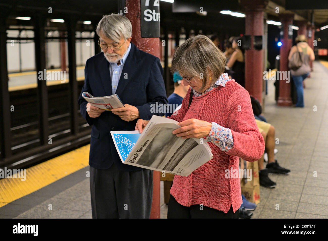 La donna la lettura del New York Times recensione libro accanto all uomo la rivista di lettura sulla metropolitana di New York, piattaforma, Manhattan, New York Foto Stock
